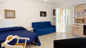 A room with a bed, a blue sofa, a chair, a desk, and a kitchenette. - Villa 'Tenuta Rosa in Salento' with Private Terrace, Private Garden and Air Conditioning (Taviano)