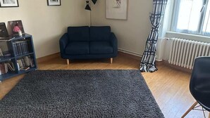 Un saló amb un sofà blau fosc, una làmpada de peu negra, una prestatgeria i un quadre amb marc a la paret.