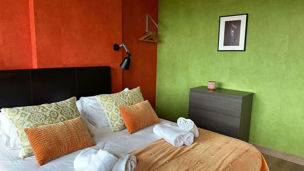 Quarto de hotel com cama, travesseiros, mesa de cabeceira com abajur, cômoda e um quadro na parede.