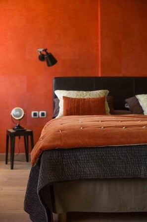 Un dormitorio con cama, mesita de noche, lámpara y aplique de pared.