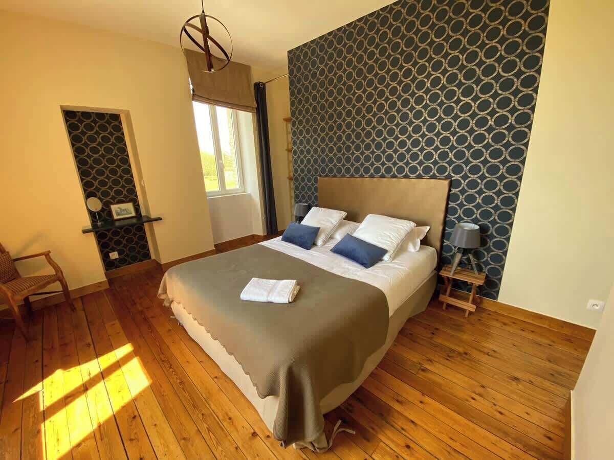 A bedroom with a large bed, a bedside table, a chair, and a window.