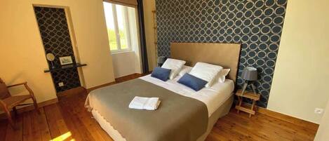 A bedroom with a large bed, a bedside table, a chair, and a window.