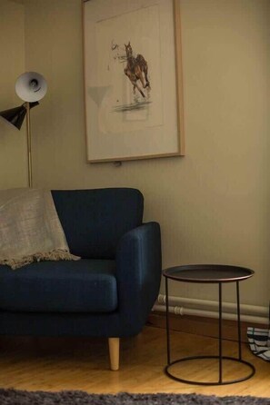 Una habitación con un sofá azul, una mesita redonda y un cuadro en la pared.