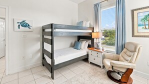 Et soveværelse med køjeseng, et sengebord med lampe, en stol og et vindue med gardiner.