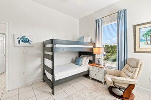 Ein Schlafzimmer mit Etagenbett, Nachttisch mit Lampe, Stuhl und einem Fenster mit Vorhängen.