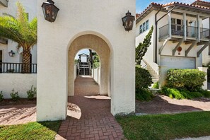 A pathway leading through an arched entrance with a brick-paved walkway, flanked by white buildings with balconies and outdoor lighting fixtures. - 5BR 30A Beach House w Gulf Views & Private Beach Access ~ Sleeps 10 (Santa Rosa Beach)