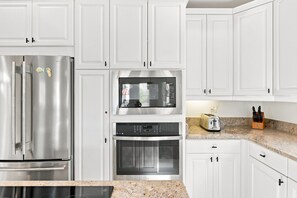 Eine moderne Küche mit weißen Schränken, Edelstahlgeräten wie Kühlschrank, Mikrowelle und Backofen sowie einer Arbeitsplatte aus Granit.