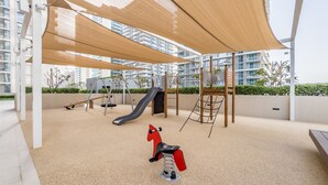 Un parque infantil con un tobogán, columpios y un caballito mecánico rojo.