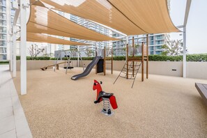 Ein Spielplatz mit Rutsche, Schaukeln und einem spielzeugroten Pferd zum Aufsitzen.