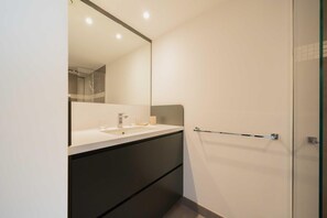Un baño moderno con un espejo grande, un lavabo y una cabina de ducha de vidrio.