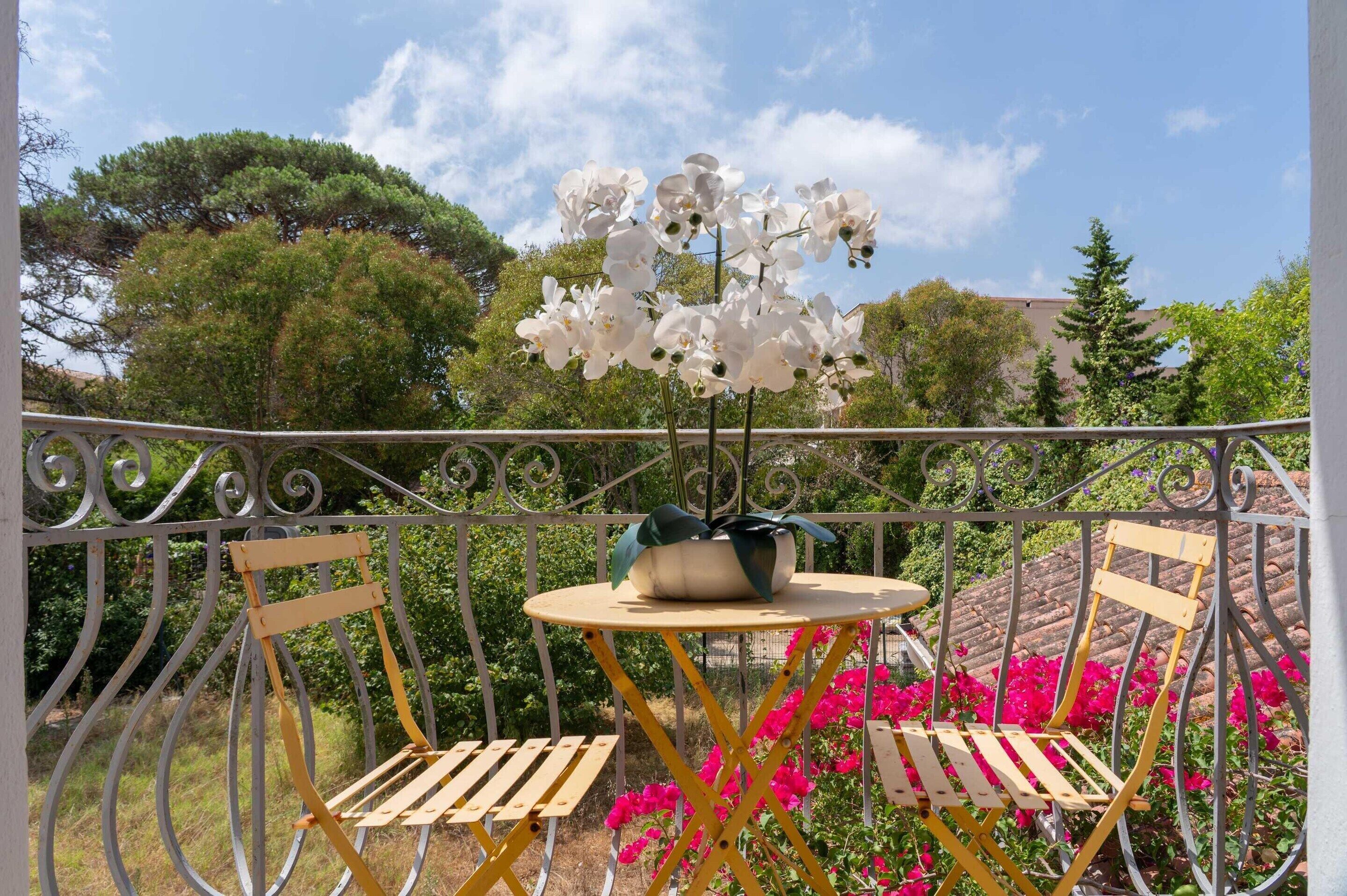 A balcony with a table and chairs, surrounded by greenery and flowers.