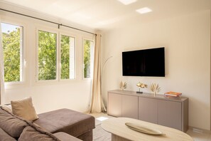 Una sala de estar moderna con un sofá, un televisor de pantalla plana en la pared y una ventana con cortinas.