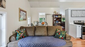 A living room with a sofa, a dining table, a bookshelf, and a kitchen area with appliances. - Pet-Friendly Above Garage Suite - Shared Hot Tub (Clarendon)