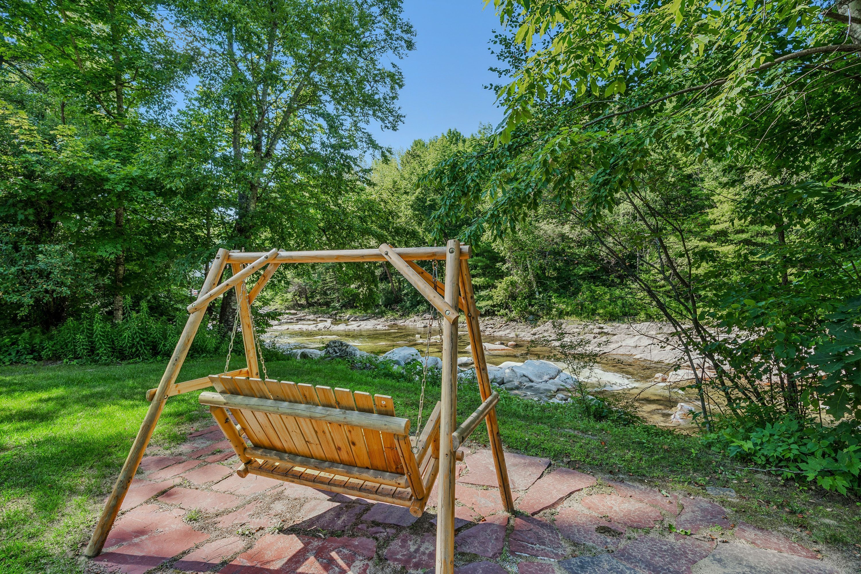 A wooden swing set in a natural setting with a stream and greenery in the background.