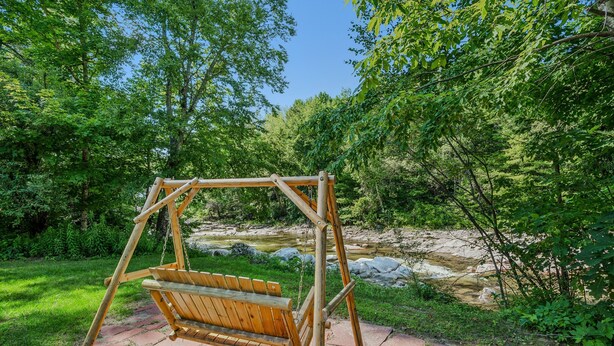 A wooden swing set in a natural setting with a stream and greenery in the background. - Pet-Friendly Above Garage Suite - Shared Hot Tub (Clarendon)