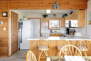A kitchen with wooden cabinets, a white countertop, and a dining area with wicker chairs. - Blue Horizon - Oceanfront Home (Atlantic Beach)