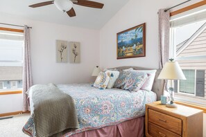Quarto com uma cama, mesa de cabeceira, abajur, ventilador de teto e um quadro na parede.