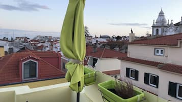 Un balcón con una sombrilla verde, una planta en maceta y vistas de un paisaje urbano con edificios de tejados rojos.