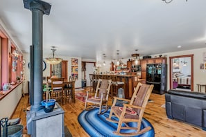 A spacious living area with a central fireplace, wooden flooring, and a dining area with a chandelier. - Country Suite | Large Deck, Hot Tub, Pet Friendly (Clarendon)