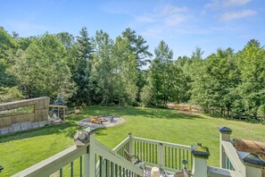 A spacious backyard with a stone fire pit, outdoor seating, and a wooden deck overlooking a forested area. - Country Suite | Large Deck, Hot Tub, Pet Friendly (Clarendon)