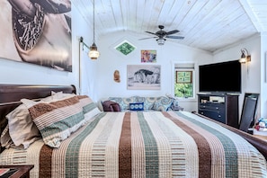 A bedroom with a large bed, a ceiling fan, artwork on the walls, and a television. - Country Suite | Large Deck, Hot Tub, Pet Friendly (Clarendon)