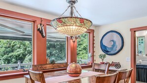 Ein Essbereich mit Holztisch und Stühlen, einer Deckenleuchte aus Buntglas und Blick ins Grüne.