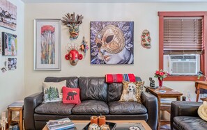 Ein Wohnzimmer mit einer Ledersofa, gerahmten Kunstwerken, dekorativen Masken und einem Fenster mit Jalousien.