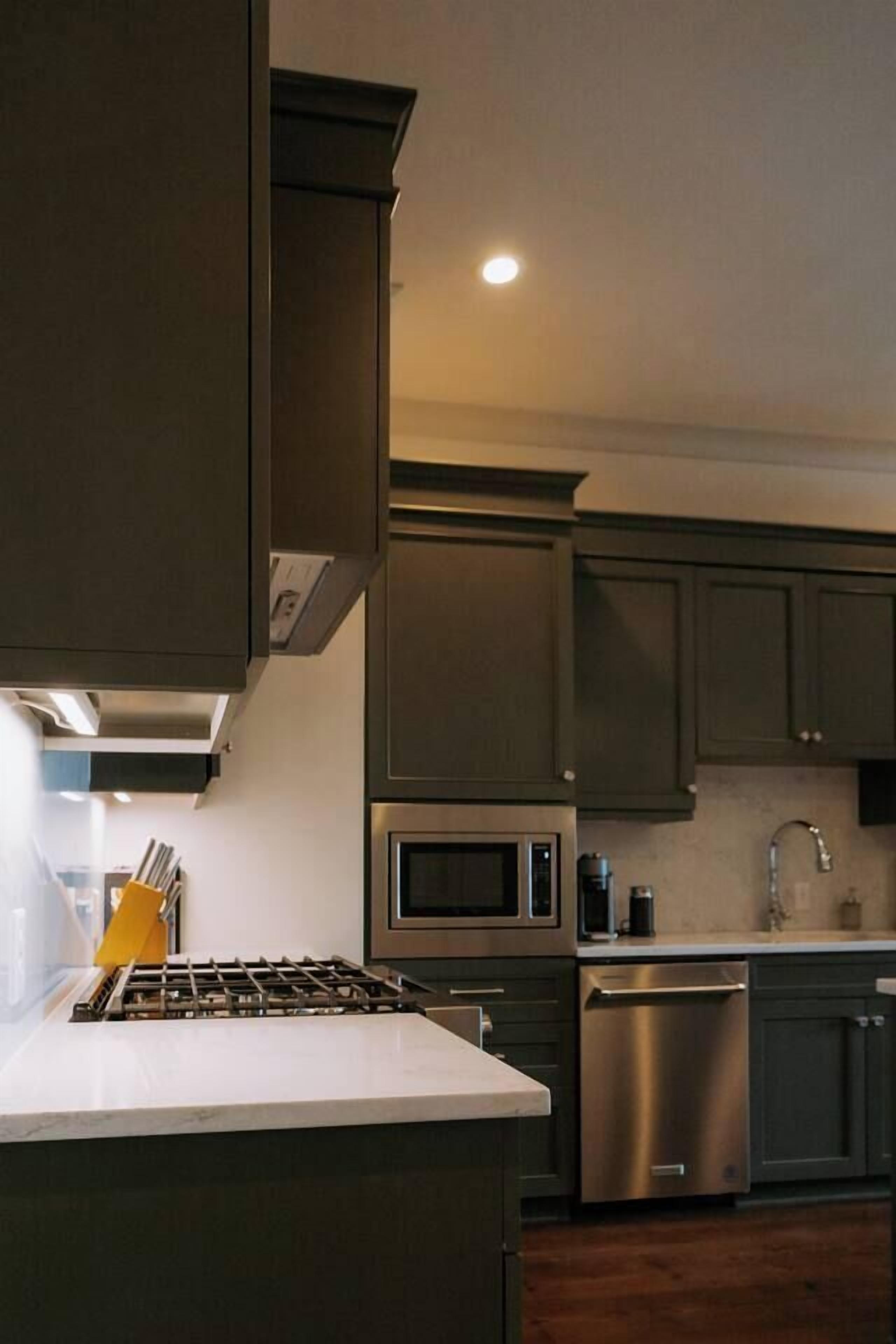 Cocina moderna con armarios oscuros, electrodomésticos de acero inoxidable y encimera blanca.