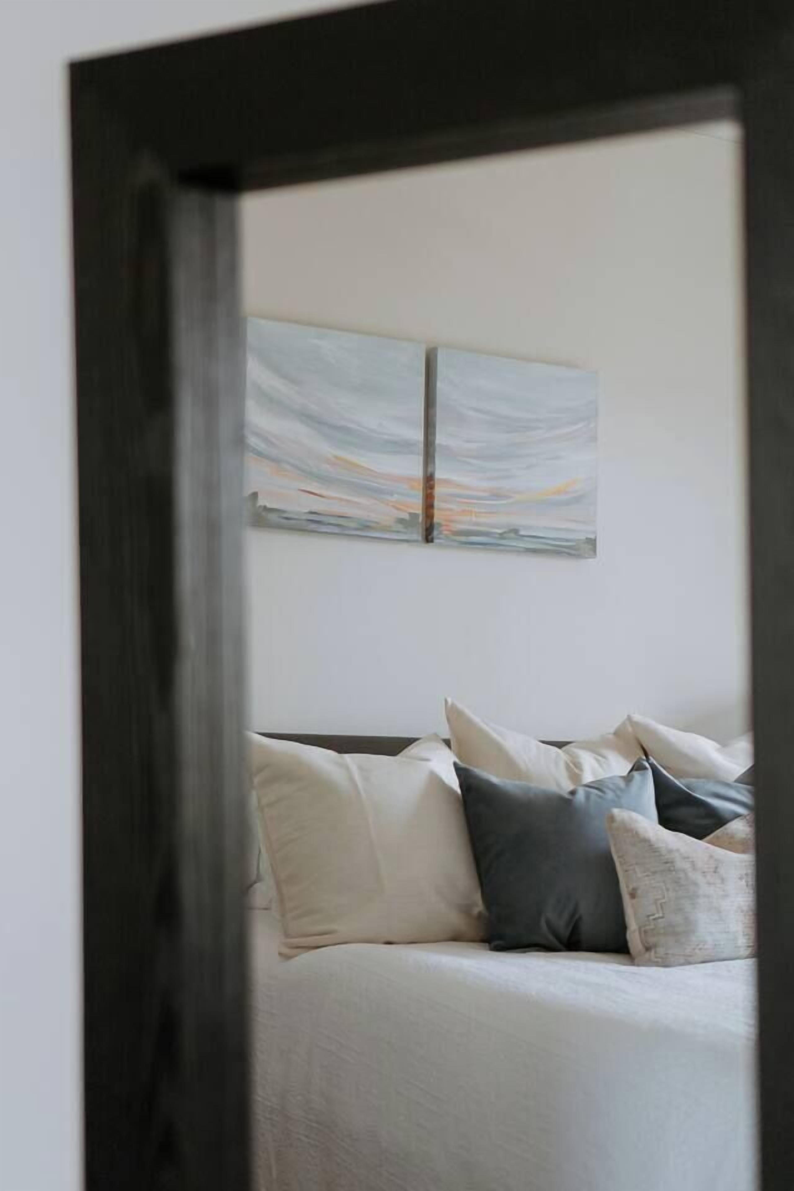 Un dormitorio con una cama, almohadas y una obra de arte colgada en la pared.