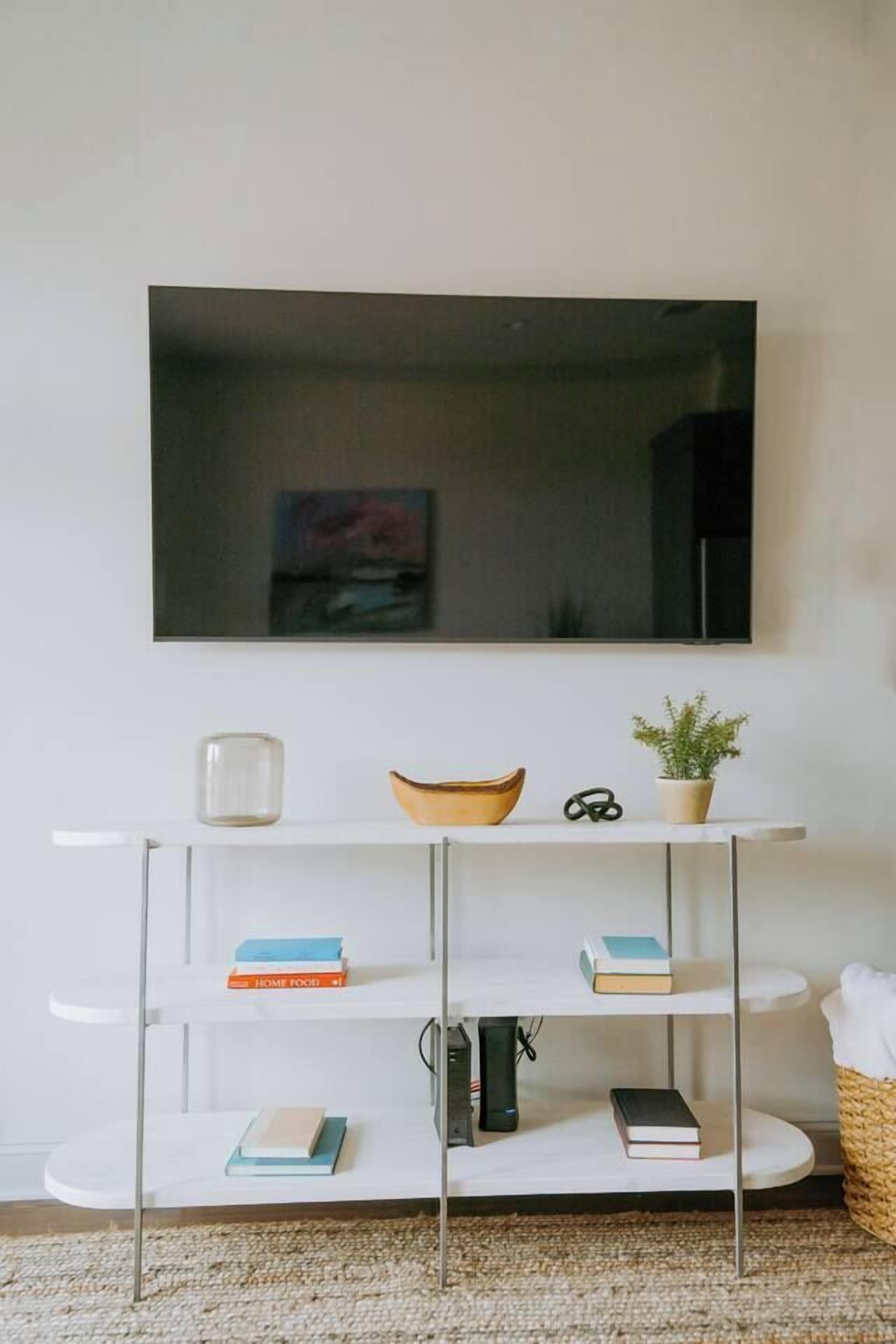 A white TV stand with shelves holding books and a bowl.