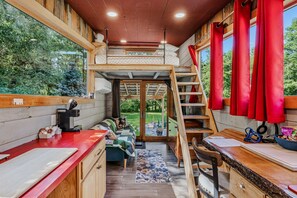 A compact, multi-level cabin with a kitchenette, a dining area, and a view of the surrounding forest. - Tiny House Getaway - Pet Friendly & Riverfront (Clarendon)