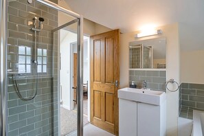 A bathroom with a glass shower enclosure, a wooden door, a sink with a mirror, and tiled walls. - Charming Dorset Coach House for 6 (Lyme Regis)