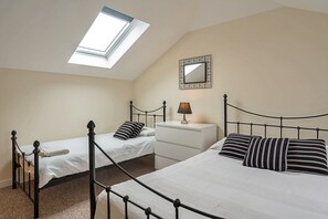 A bedroom with two single beds, a nightstand with a lamp, a mirror, and a skylight. - Charming Dorset Coach House for 6 (Lyme Regis)