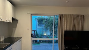 Hotellihuone, jossa on sänky, televisio, pieni keittiö ja liukuovet, joista pääsee ulos.