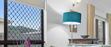 Un salon avec un canapé vert, un vase décoratif et une vue sur l’extérieur, visible à travers une grande fenêtre.