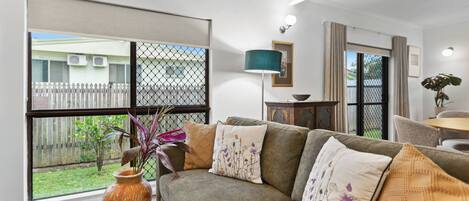 A living room with a sofa, a vase, and a view of a fenced backyard.
