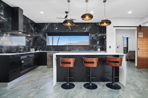 A modern kitchen with a central island, black cabinets, marble backsplash, and pendant lighting. - Luxury Northcrest Retreat with Pool | Sleeps 7 (Berrimah)