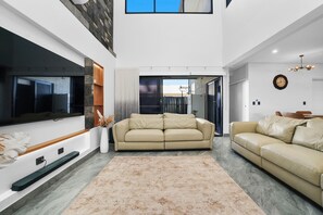 A modern living room with a large flat-screen TV, two beige sofas, a patterned rug, and a stone accent wall.