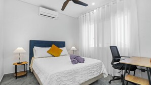 A hotel room with a bed, a desk, a chair, a ceiling fan, and an air conditioning unit.