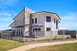 A modern two-story house with a covered patio, a stone chimney, and a fenced yard. - Luxury Northcrest Retreat with Pool | Sleeps 7 (Berrimah)