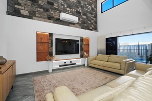 Ein modernes Wohnzimmer mit einer Wand aus Naturstein, einem Flachbildfernseher, einem beigefarbenen Sofa und einem großen Fenster.