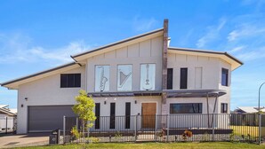 A modern two-story house with a garage, a fenced yard, and a clear blue sky.