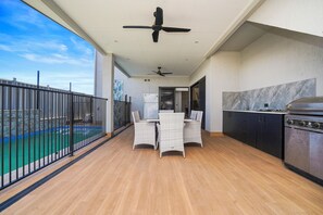Varanda com piscina, mesa de jantar com cadeiras, ventiladores de teto e área de cozinha.
