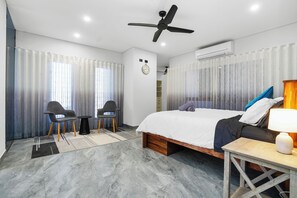 A modern hotel room with a bed, a desk, two chairs, a ceiling fan, and an air conditioning unit. - Luxury Northcrest Retreat with Pool | Sleeps 7 (Berrimah)