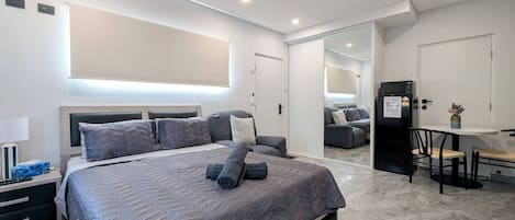 A modern bedroom with a large bed, a ceiling fan, a built-in desk, and a refrigerator.
