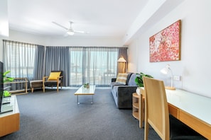A modern living room with a sofa, armchair, coffee table, and a painting on the wall. - Darwin City Sights Apt | Big Pool and FREE parking (Darwin City)