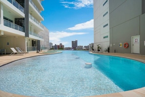 A swimming pool with clear water, surrounded by modern buildings, and a view of the city skyline in the background. - Darwin City Sights Apt | Big Pool and FREE parking (Darwin City)