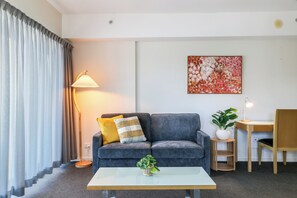 A modern living room with a grey sofa, a small table, a lamp, and a painting on the wall. - Darwin City Sights Apt | Big Pool and FREE parking (Darwin City)