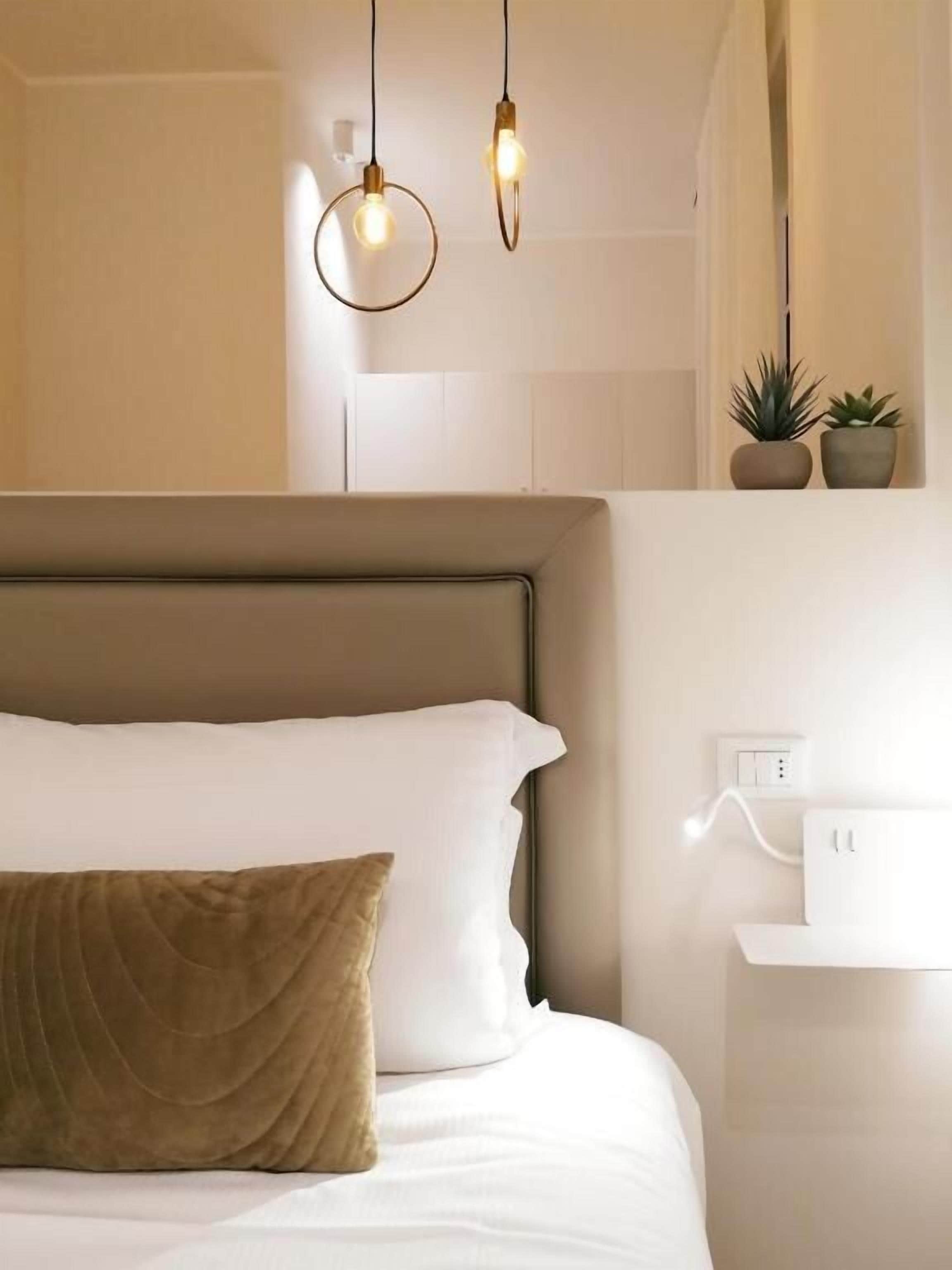 A neatly made bed with a headboard, a brown pillow, and two wall-mounted light fixtures.