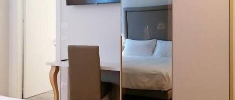 Una habitación de hotel con cama, escritorio, silla, televisor y armario.